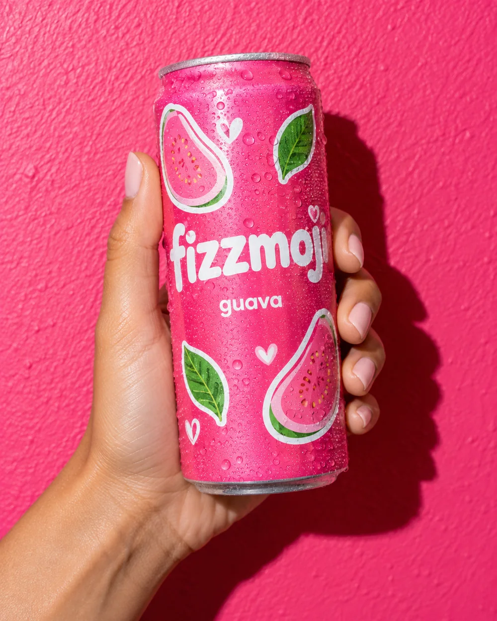 A hand holding a chilled pink guava Fizzmoji against a hot-pink wall